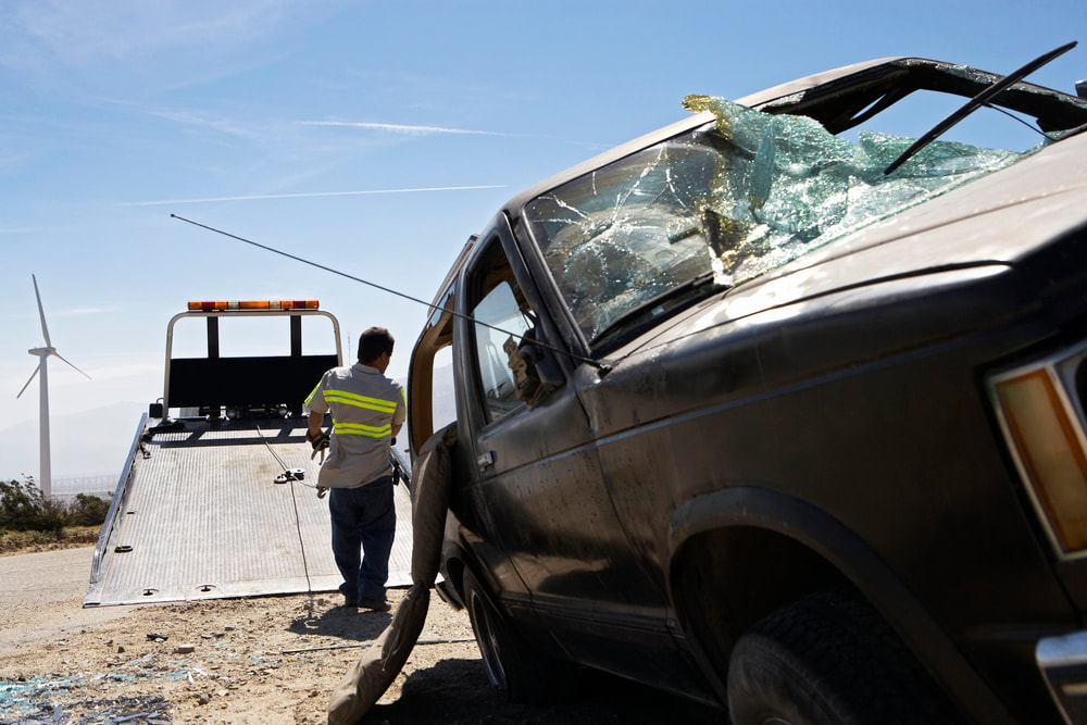 A man preparing to lift a crashed car onto a tow truck. 